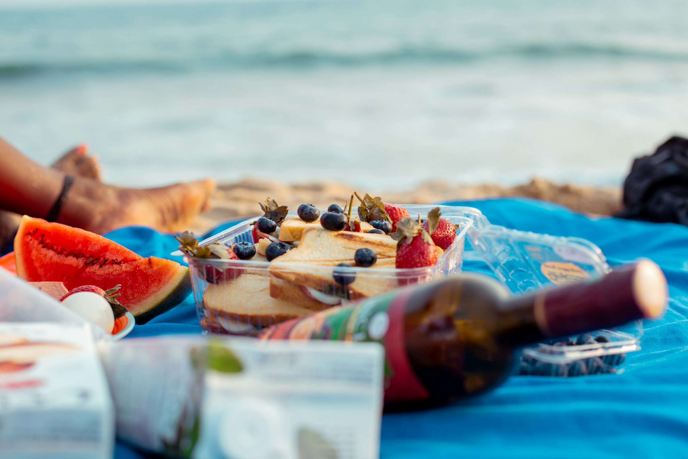 Photo by Tobias Nii Kwatei Quartey on Unsplashed - beach picnic with brown bottle and sandwiches 